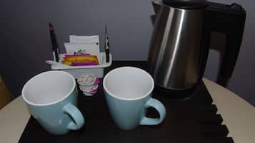 A table with two light blue cups, a small container with a colorful lid, and a stainless steel electric kettle.