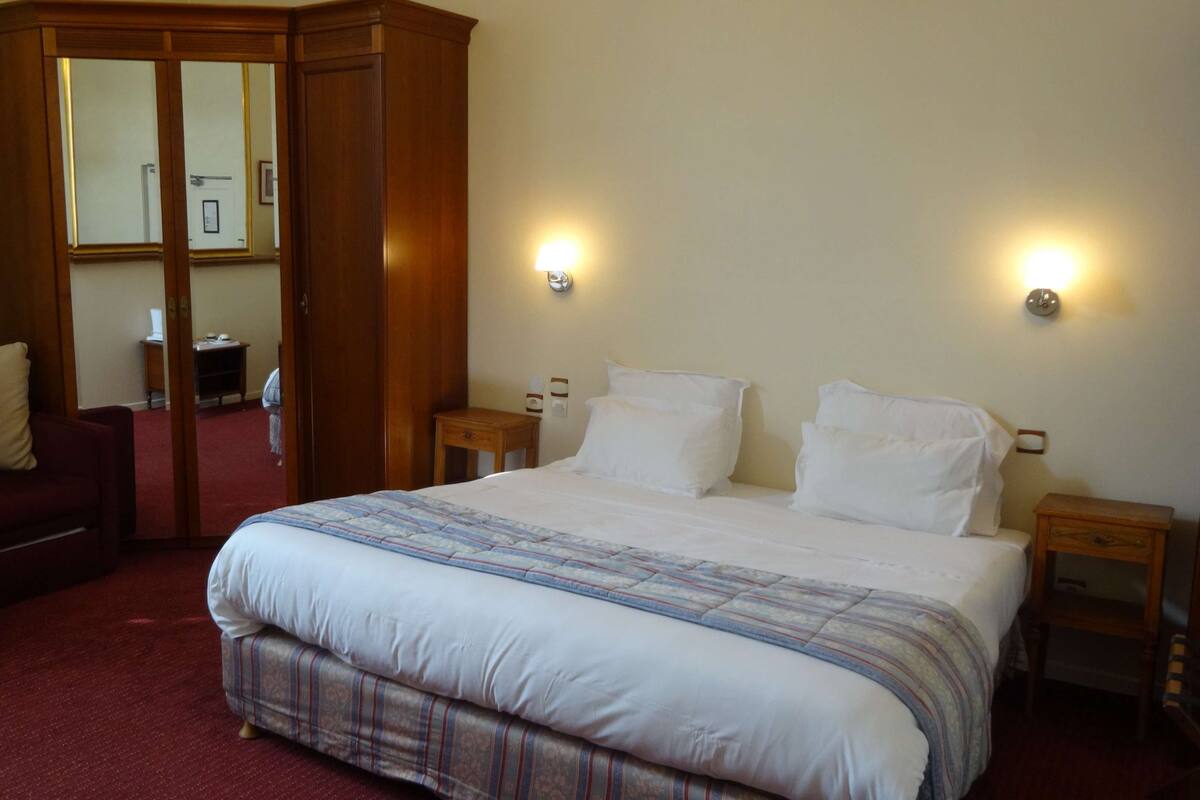 A hotel room with a large bed, a wooden wardrobe, a red sofa, and two bedside tables with lamps.