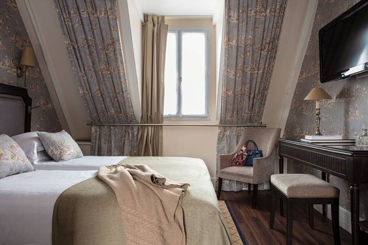 A bedroom with a bed, a chair, a desk, and a TV.