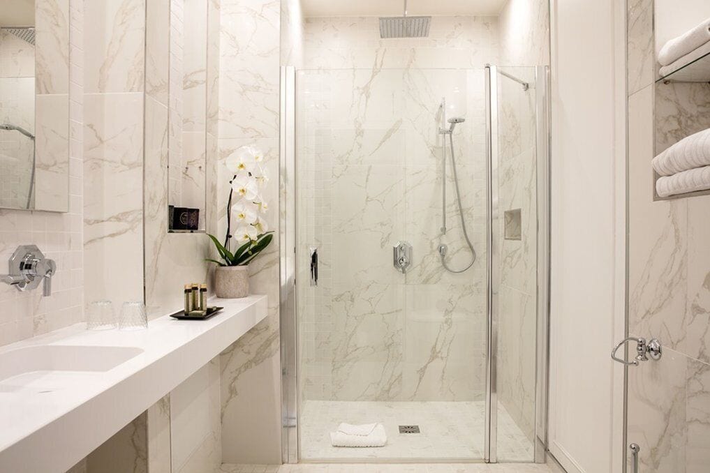 A modern bathroom with a glass-enclosed shower, marble walls, a white sink, and a small potted orchid.