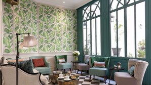 A room with a checkered floor, green upholstered chairs, a lamp, and a window with a view of greenery. - Hôtel Serotel Lutèce (Paris)