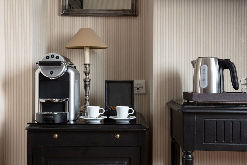 Une petite cuisine équipée comprenant une machine à café, deux tasses, une bouilloire et une lampe, le tout posé sur une table en bois foncé.