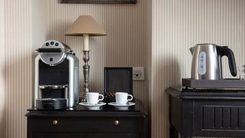 Une petite cuisine équipée comprenant une machine à café, deux tasses, une bouilloire et une lampe, le tout posé sur une table en bois foncé.