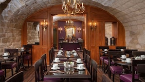 A dining area with a long table set for a meal, surrounded by chairs, in a room with stone walls and wooden paneling. - Hôtel Serotel Lutèce (Paris)