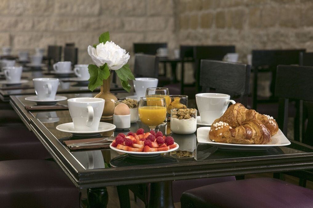 Mesa posta para o café da manhã, com um croissant, frutas, suco de laranja e xícaras de café.