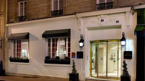 A hotel entrance with a glass door, a number sign above the door, and two potted plants on the sidewalk. - Hôtel Serotel Lutèce (Paris)