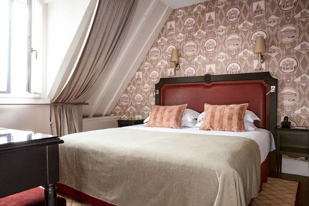 Una habitación de hotel con una cama grande, una mesita de noche, una lámpara y una ventana con cortinas.