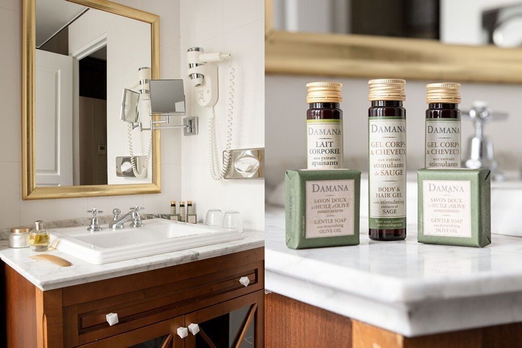 A bathroom with a white sink, a mirror, and a telephone. There are three bottles of Damana body and hair gel on the counter.