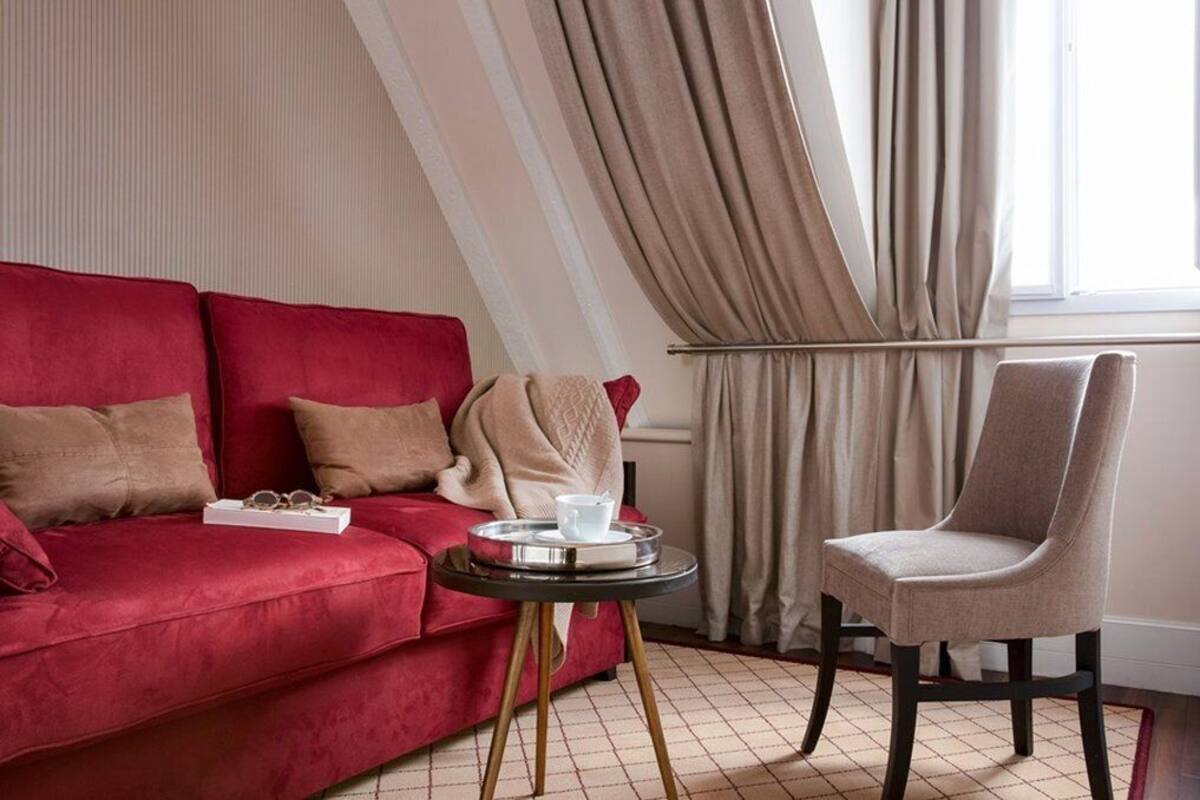A red sofa with a tray table and a chair, a window with curtains, and a tiled floor.