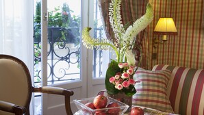A room with a striped sofa, a glass table with a bowl of apples, a vase with flowers, and a lamp.