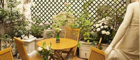 Une table ronde en bois, des chaises, une statue et des plantes en pot.