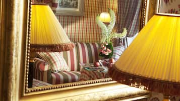 A room with a striped sofa, a glass coffee table with apples, and a mirror reflecting lamps and curtains.