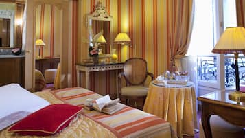 A hotel room with a bed, a desk with a lamp, a chair, and a table with a tray of items.
