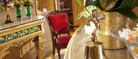 A room with a marble-topped table, a red chair, and a gold bell.