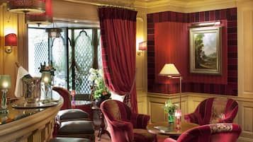 A luxurious room with a red and gold color scheme, featuring a large window with curtains, a painting on the wall, and a seating area with a table and chairs.