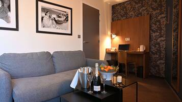 A modern living room with a grey sofa, a dining area with a wooden table and chairs, and a small kitchen area.