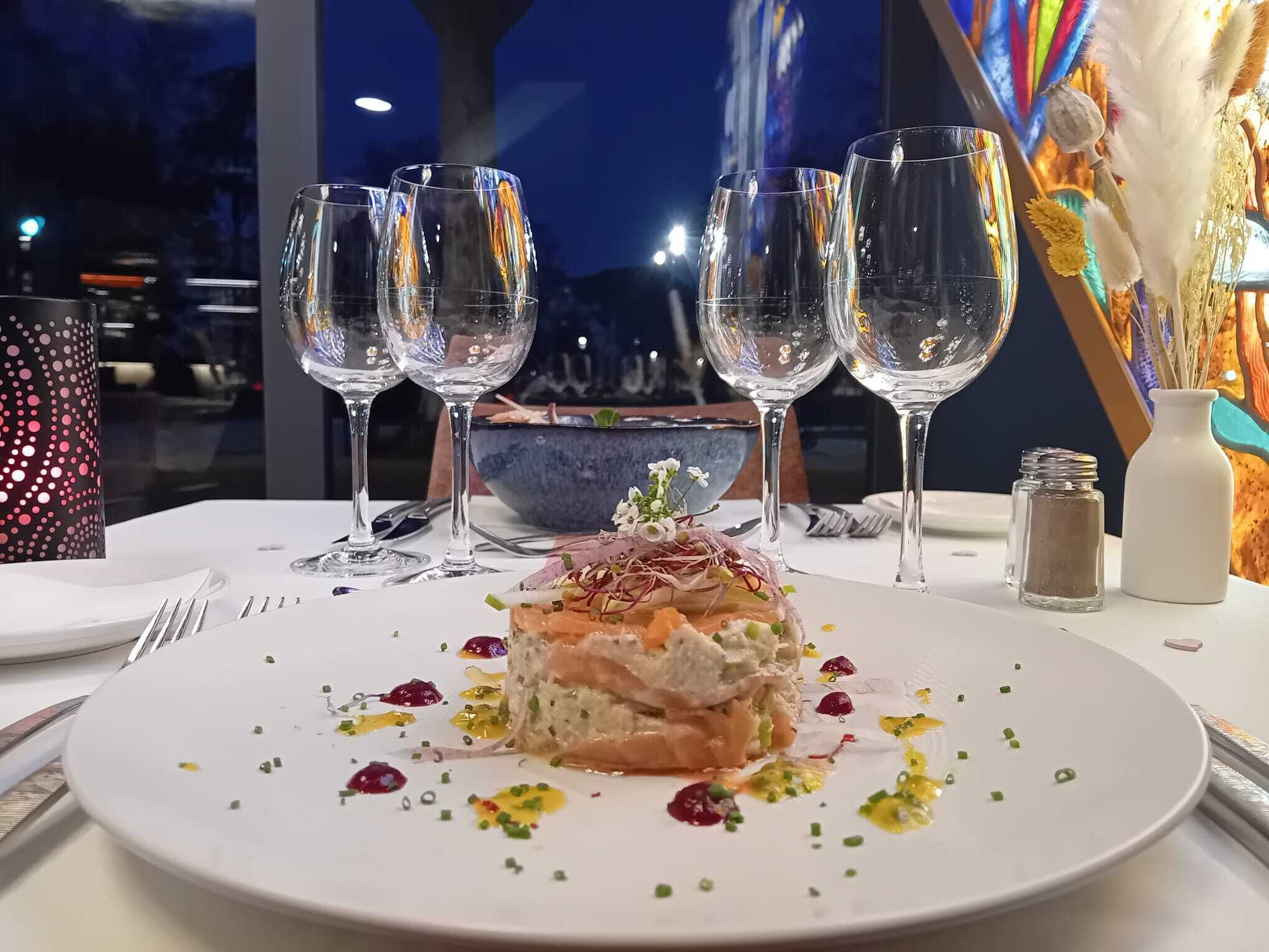 Une table à manger avec une assiette blanche remplie de nourriture, deux verres à vin et un vase décoratif.