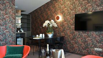 A modern living room with a floral wallpaper, a flat-screen TV, a dining area with a table and chairs, and a red armchair.