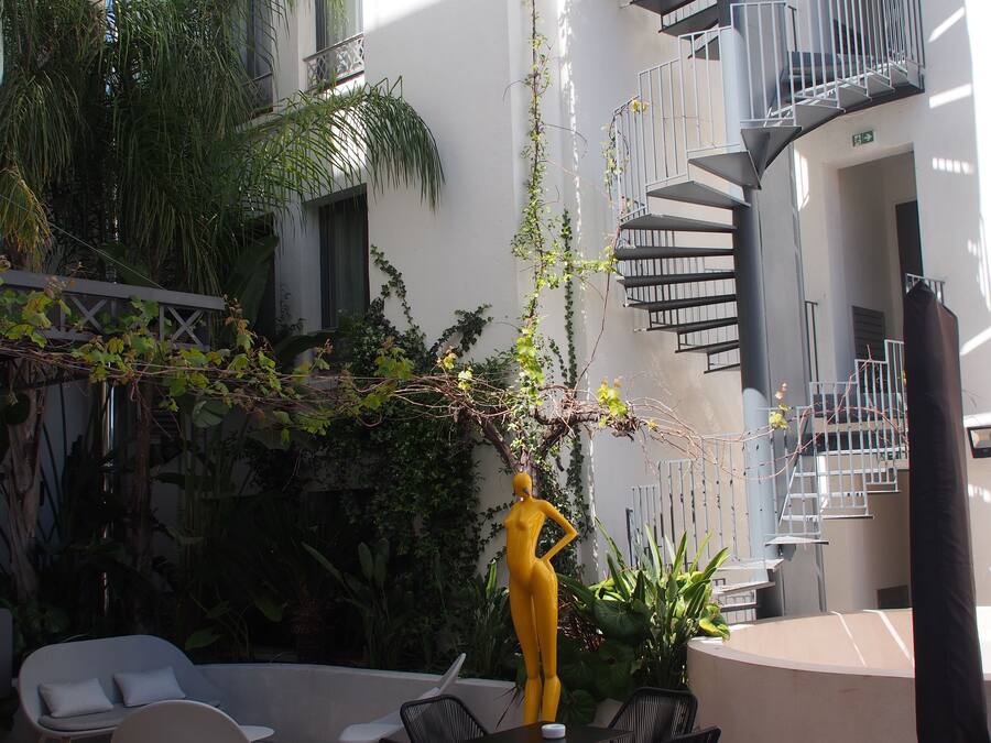 Un espacio exterior moderno con una escultura amarilla, una escalera en espiral y una zona de estar con sillas y una mesa.