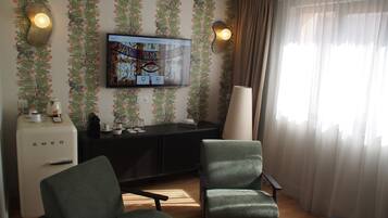 Una sala de estar con un televisor de pantalla plana montado en la pared, dos sillones, una cafetera y una lámpara.