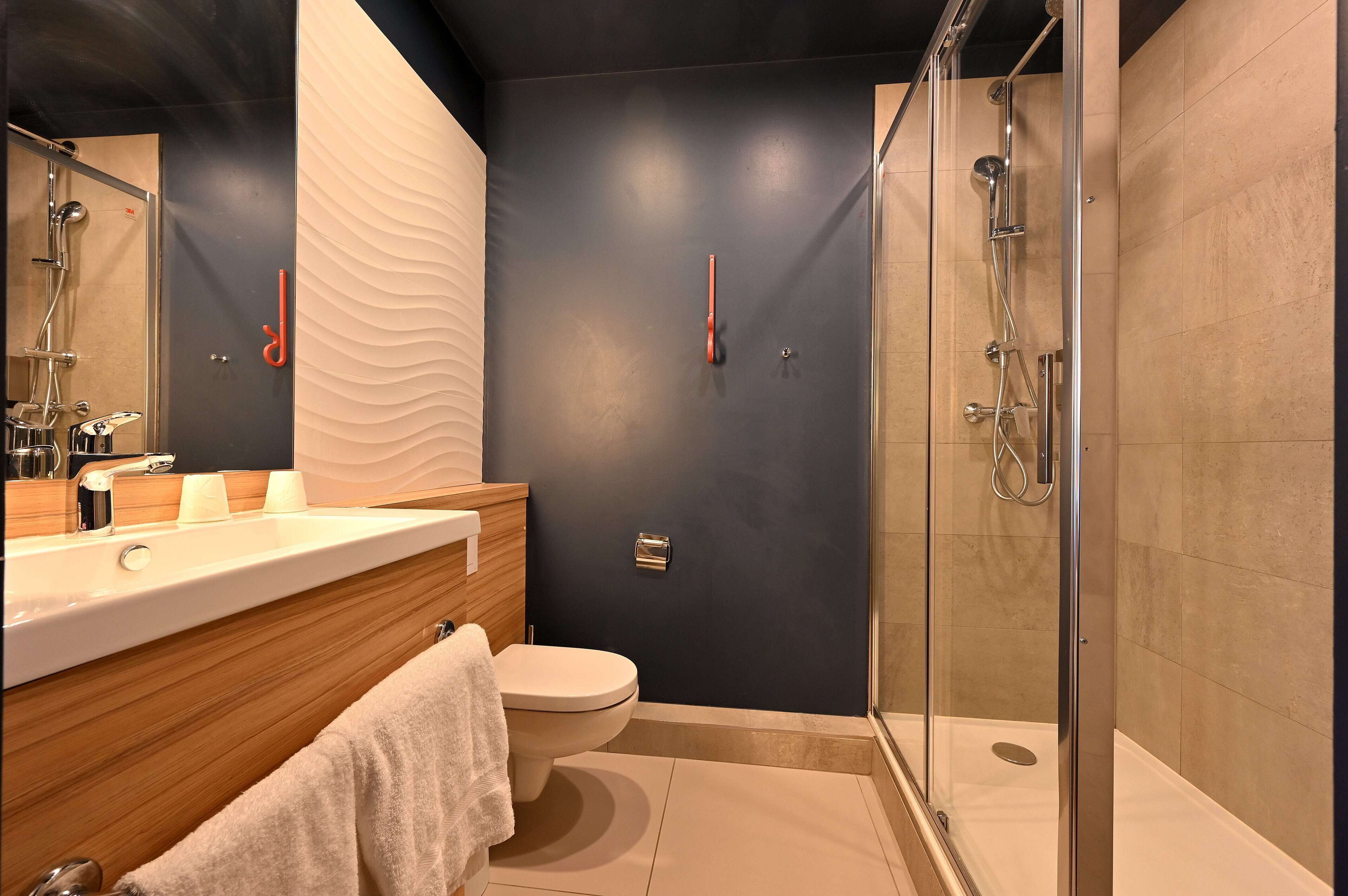 A modern bathroom with a glass-enclosed shower, a wooden vanity, and a white toilet.