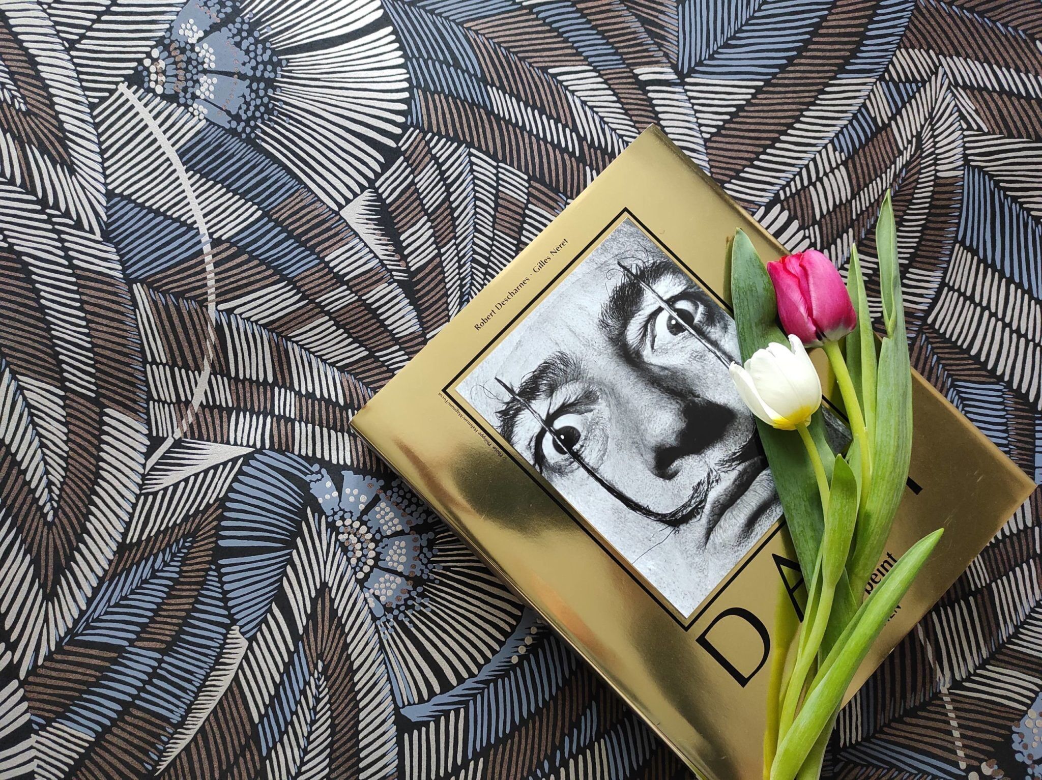 A book titled 'Robert Deschamps - Gilles Net' with a black and white illustration, placed on a patterned fabric background.