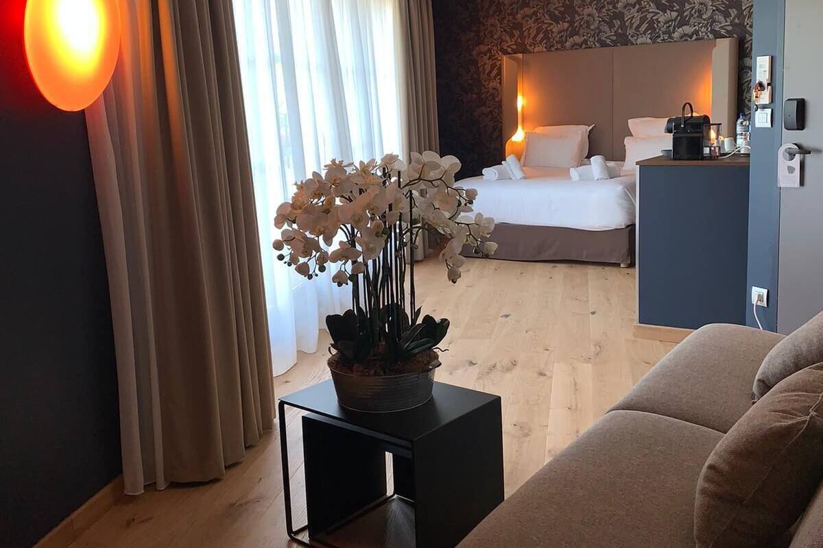 Habitación de hotel con cama, zona de estar con sofá, una mesita con una planta y un escritorio con lámpara.