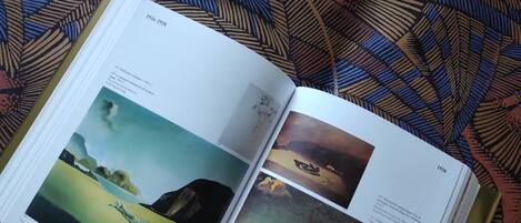 An open book with pages displaying artwork and text, placed on a patterned fabric background.