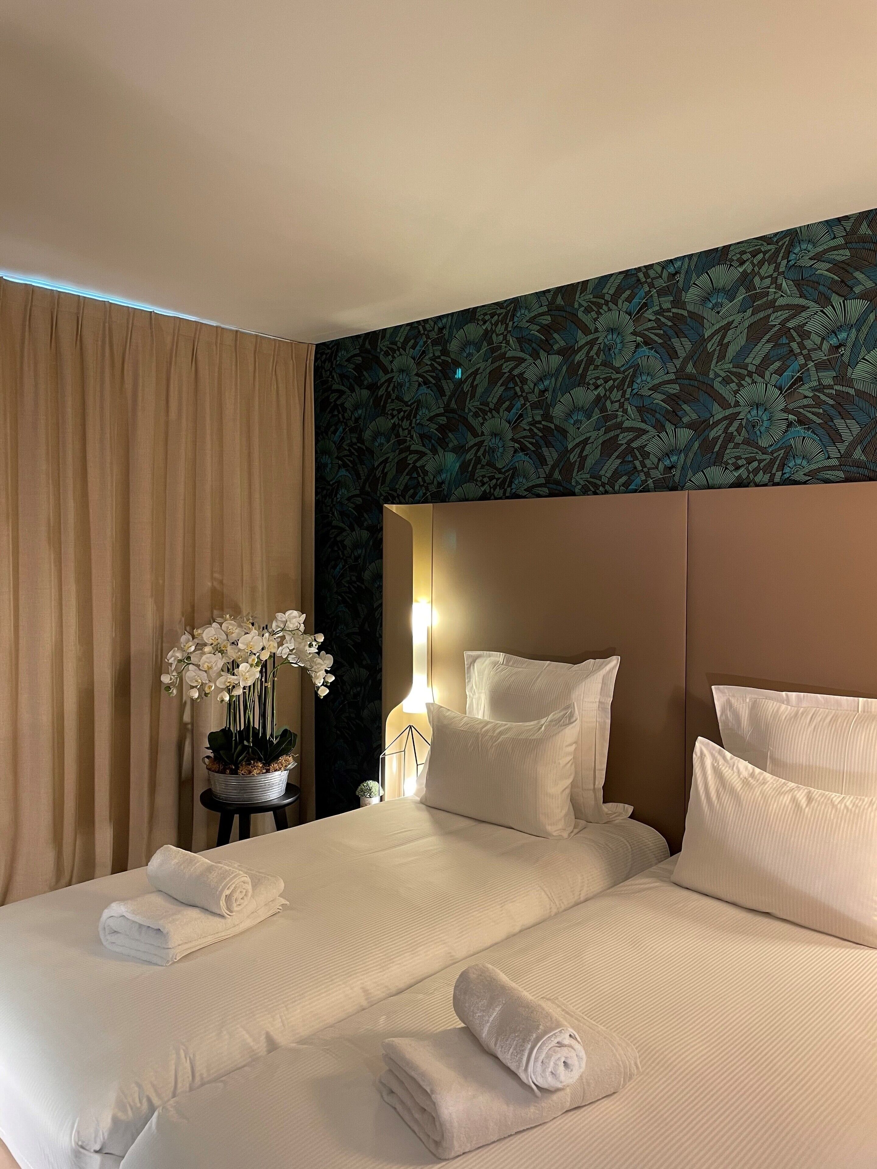 Habitación de hotel con cama, almohadas, mesita de noche con lámpara y una orquídea en maceta.
