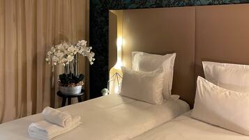 Habitación de hotel con cama, almohadas, mesita de noche con lámpara y una orquídea en maceta.