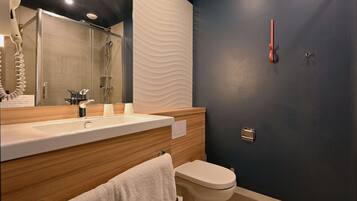 A modern bathroom with a wooden vanity, a white sink, a mirror, a toilet, and a shower area.