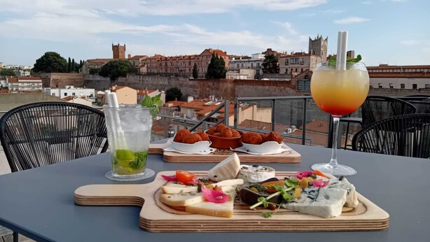 A table with a variety of food items and a drink, set against a backdrop of a cityscape with historical buildings.