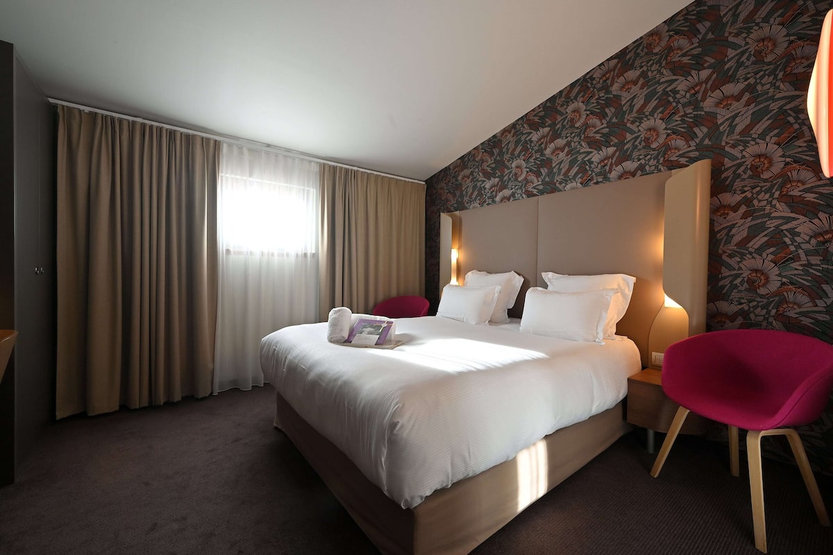 Una habitación de hotel con una cama grande, una silla roja y un papel tapiz floral.