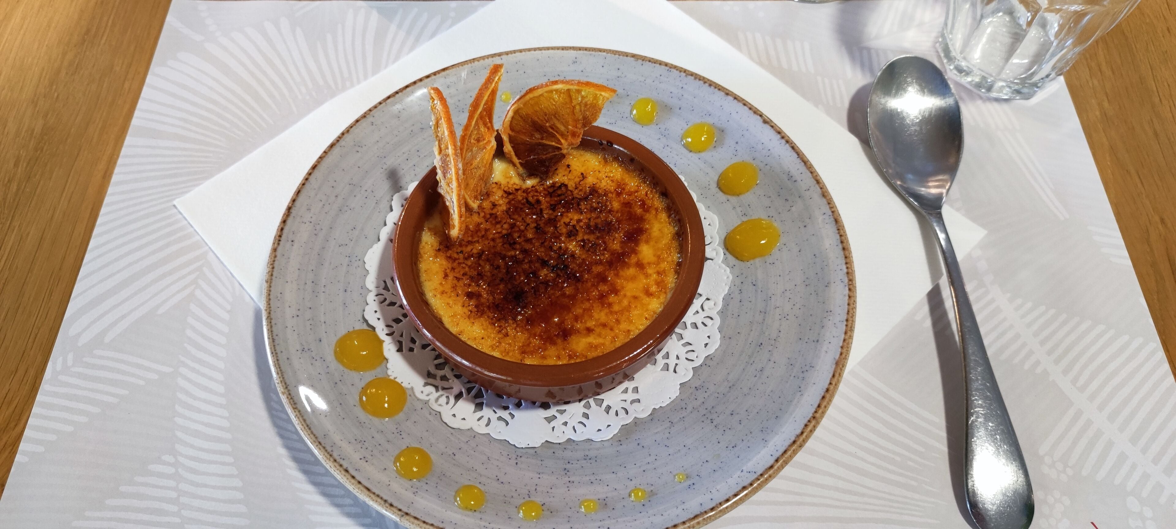 Un postre en un plato con una cuchara y un vaso de agua sobre una mesa.