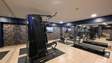 Un gimnasio con equipo de ejercicio, incluyendo cintas de correr y una máquina de pesas, y un muro con espejos.