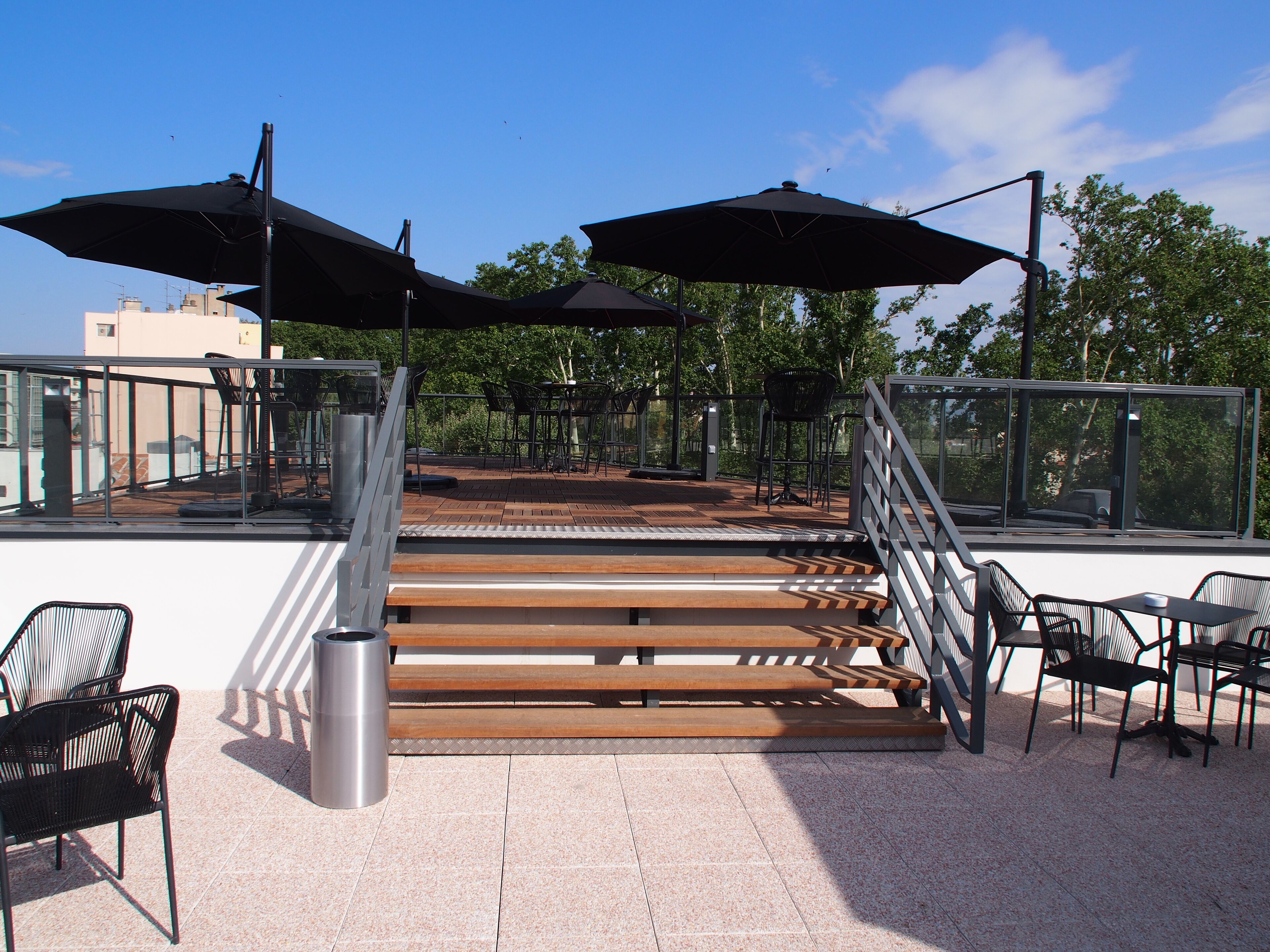 Terraza en la azotea con mobiliario exterior, una escalera y vistas del horizonte urbano.