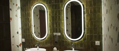 Un baño con dos lavamanos, cada uno con un espejo encima. Las paredes están cubiertas con un mosaico verde.