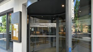 A hotel entrance with a revolving door, a welcome sign, and a small outdoor seating area visible through the glass doors.