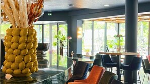 A modern restaurant interior with a curved ceiling, a central bar area with a unique yellow vase, and a seating area with dark-colored chairs.