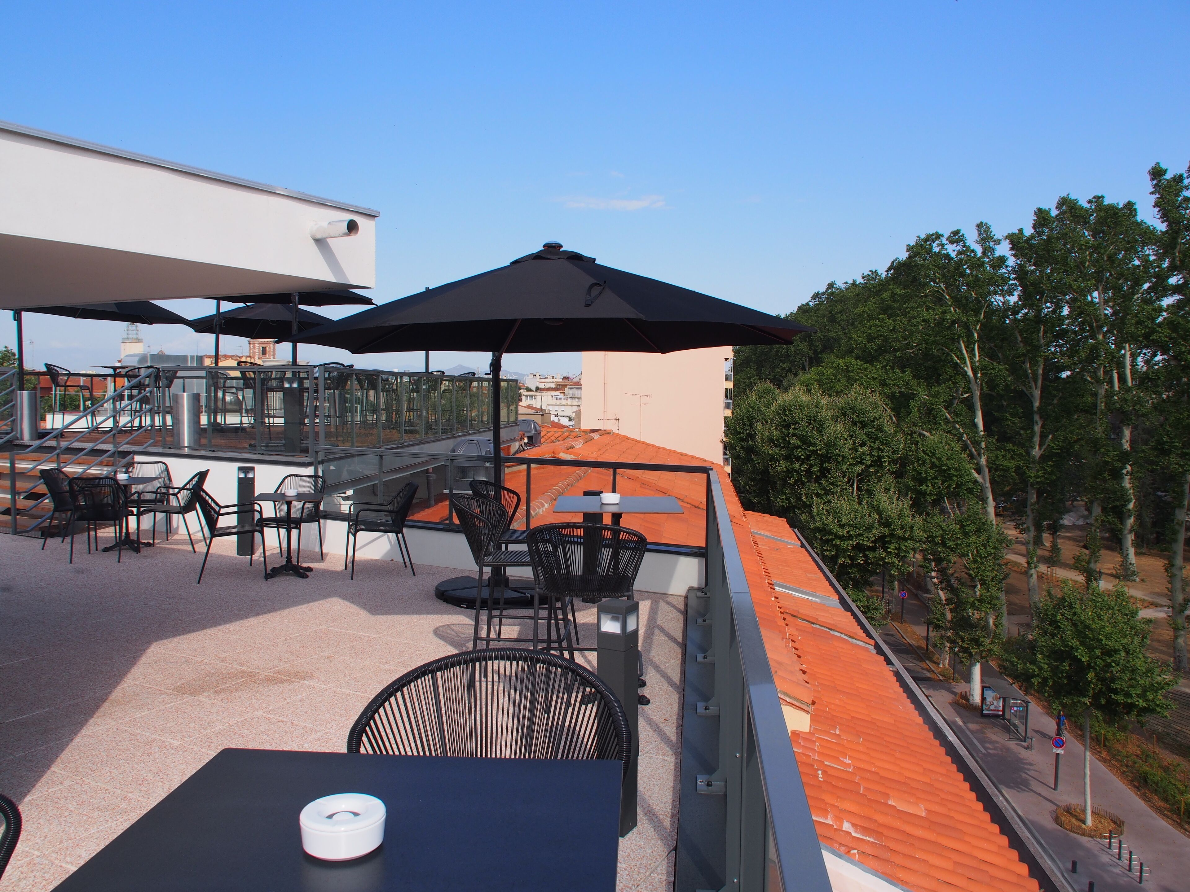 A rooftop terrace with outdoor seating, including tables and chairs, and umbrellas providing shade.