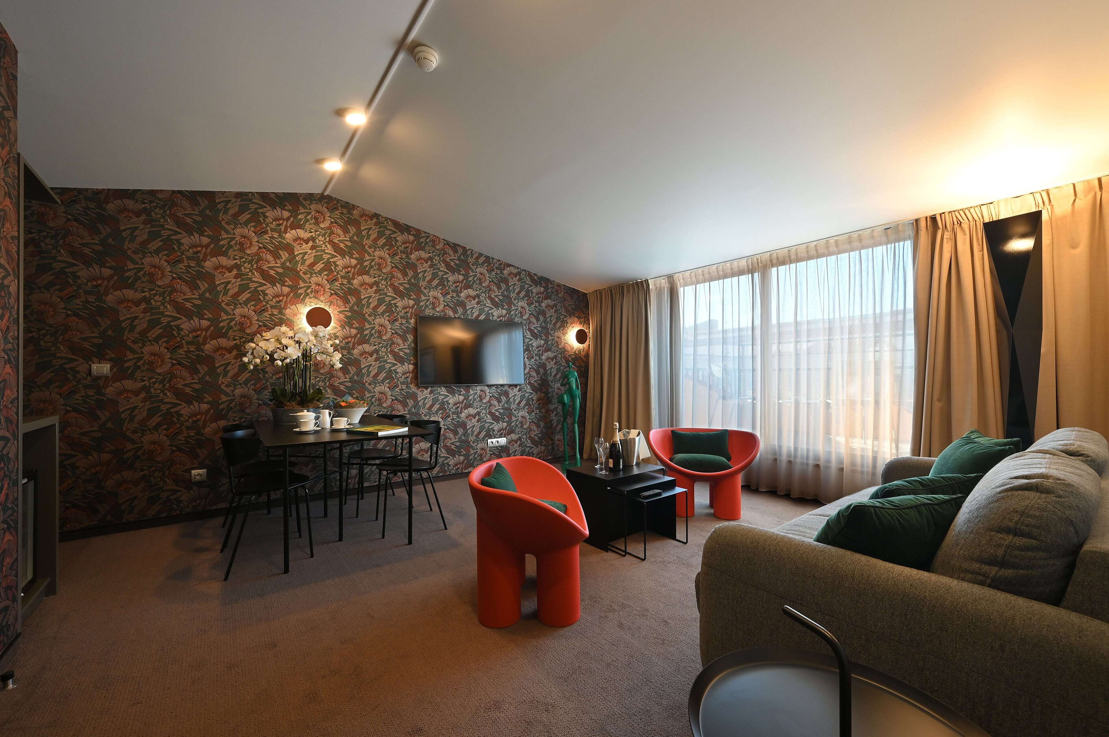 En moderne stue med en sofa, et spisebord med stole, et fjernsyn ophængt på væggen og et stort vindue med gardiner.