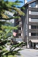 Un moderno edificio de hotel con balcones, una bandera suiza y vistas a la montaña.