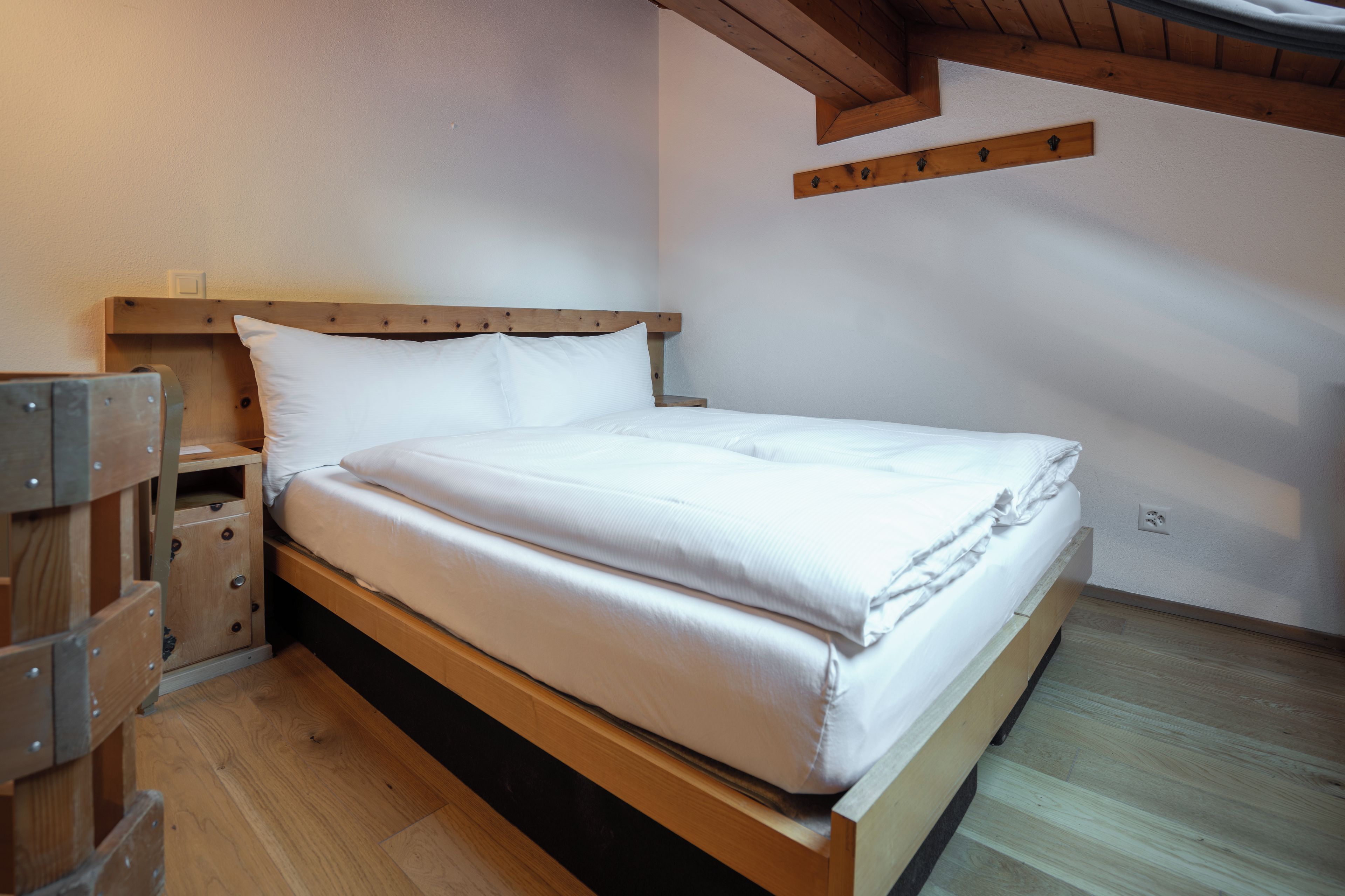 A single bed with a wooden frame and white bedding in a room with wooden flooring and a sloped ceiling.