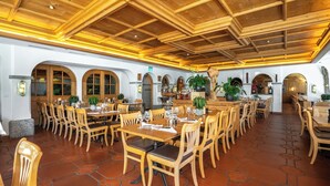 A spacious dining area with wooden tables and chairs, a tiled floor, and a wooden ceiling with exposed beams.
