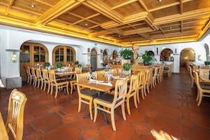 Un comedor amplio con mesas y sillas de madera, suelo de baldosas y techo de madera con vigas a la vista.