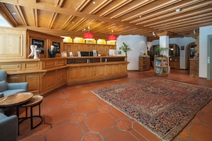 A wooden reception desk with a red pendant light, a large patterned rug, and a seating area with a round table.