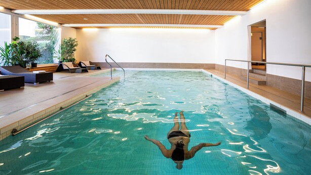 Piscina con una persona flotando, rodeada de sillas de descanso y plantas en macetas.