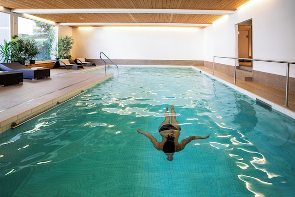 A swimming pool with a person floating, surrounded by lounge chairs and potted plants.