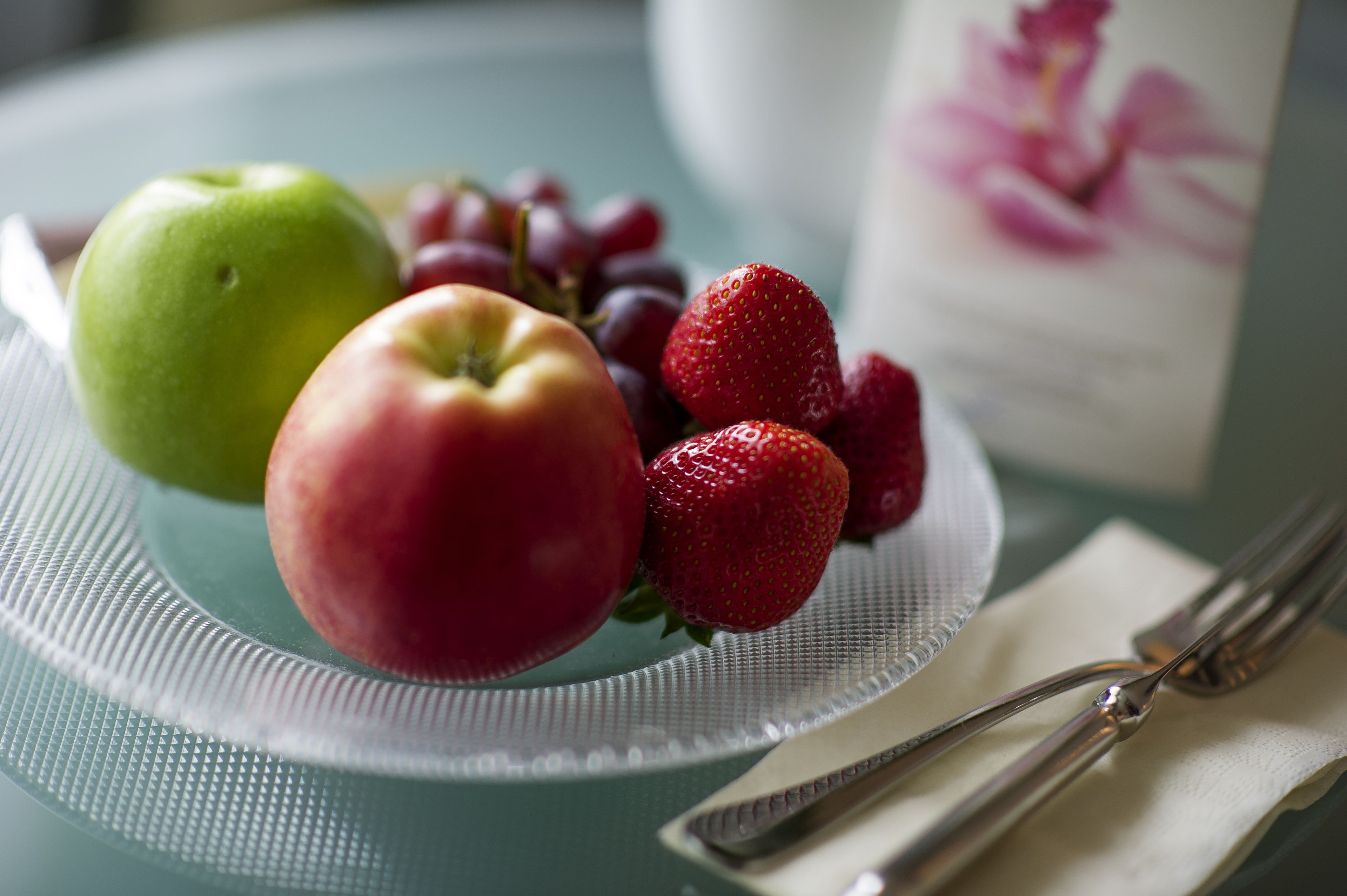 A plate with a green apple, a red apple, and strawberries on a textured tablecloth.