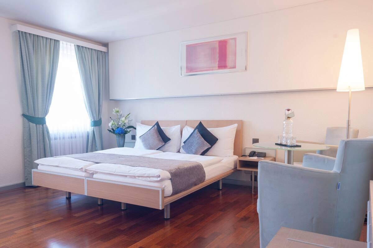 Ein Hotelzimmer mit einem Bett, einem Schreibtisch, einem Stuhl, einer Lampe und einem Bild an der Wand.